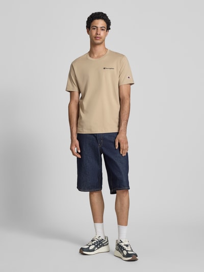 Männermodel trägt T-Shirt mit Logo-Stitchings Modell 'ICONS CONTRAST' von CHAMPION, beige, Baumwoll-Mix, Modern Fit, Ganzkörperansicht von vorne.