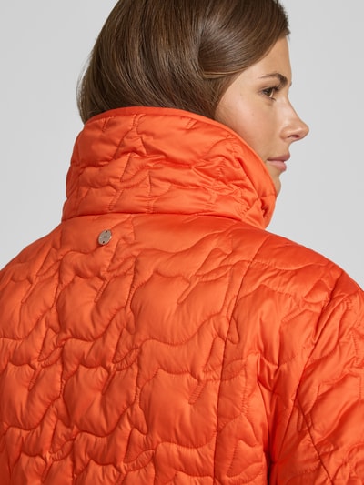 Vrouwenmodel draagt Steppjacke mit aufgesetzten Taschen und Bindegürtel van Marc Cain in feloranje met doorgestikte structuur, detailopname rug, regular fit, opstaande kraag, knoopsluiting, ruglengte maat M 70 cm, schouderbreedte 45 cm, borstwijdte 43 cm, mouwlengte 62 cm.