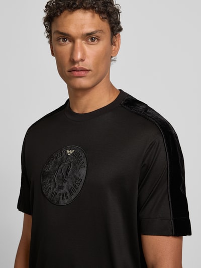 Männermodel trägt T-Shirt mit Label-Detail von Emporio Armani, schwarz, Lyocell-Baumwoll-Mix, Regular-Fit, gerippter Rundhalsausschnitt, Nahaufnahme Oberkörper.