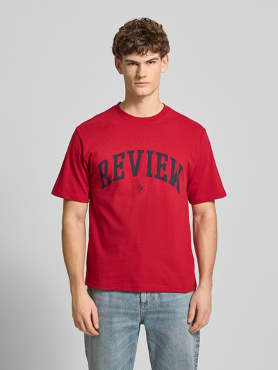 Männermodel trägt T-Shirt mit Label-Print und Rundhalsausschnitt von REVIEW in Rot mit schwarzem Print, reine Baumwolle, Ganzkörperansicht von vorne