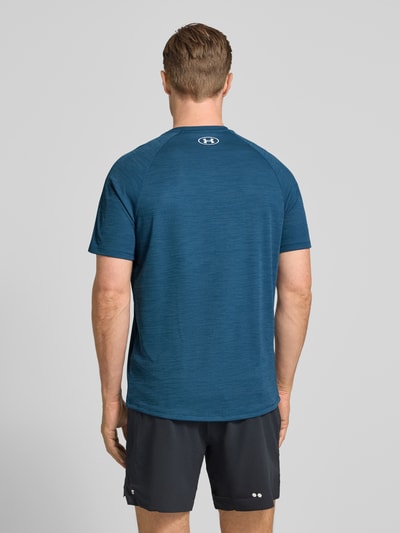 Męski model nosi męski t-shirt z nadrukiem z logo model 'Tech' od Under Armour, prosty krój, okrągły dekolt, długość tyłu w rozmiarze M: 75 cm, ciemnoniebieski kolor, struktura gładka, widok całej sylwetki z tyłu.