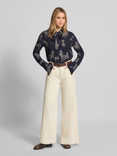 Frauenmodel trägt Relaxed Fit Bluse aus reiner Viskose Modell 'ODETTA' von ODETTA mit Allover-Motiv-Print, dunkelblau-weiß, Zierschleife, langärmelig, Ganzkörperansicht von vorne.