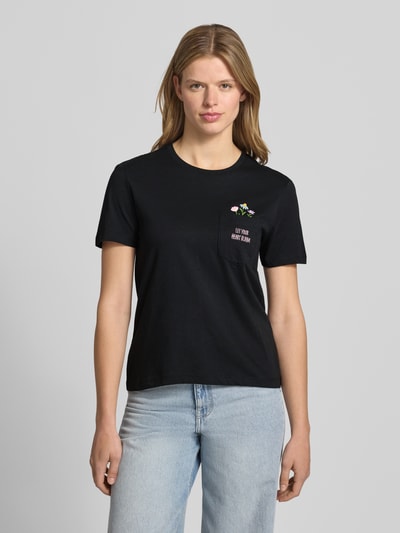 Frauenmodel trägt Regular Fit T-Shirt aus reiner Baumwolle Modell 'POLLY' von Only, Optik: Unifarben, Applikation: Stickerei, Rundhals, Kurzarm, Brusttasche, Farbe Schwarz, glatte Textur, Ganzkörperansicht von vorne.