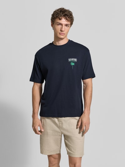 Męski model nosi T-Shirt aus Baumwolle mit rückseitigem Print od MCNEAL, kolor granatowy, krój relaxed fit, bawełna, przód, ujęcie całopostaciowe z przodu.