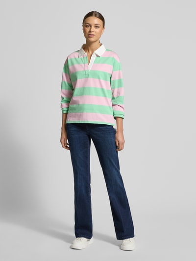 Frauenmodel trägt Regular Fit Poloshirt aus reiner Baumwolle von s.Oliver RED LABEL, gestreift in Rosa und Grün, Piqué-Struktur, Polokragen mit V-Ausschnitt, langarm, Rumpfabschluss mit Seitenschlitzen, ganzkörperansicht von vorne.