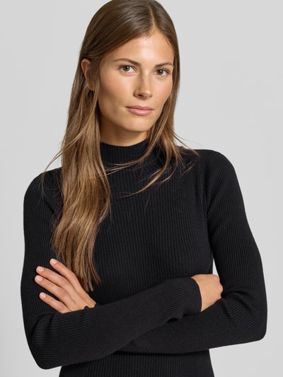 Frauenmodel trägt Strickkleid aus Viskose-Mix in Midilänge von MYON, schwarze Ripp-Optik, Stehkragen, Nahaufnahme Oberkörper.