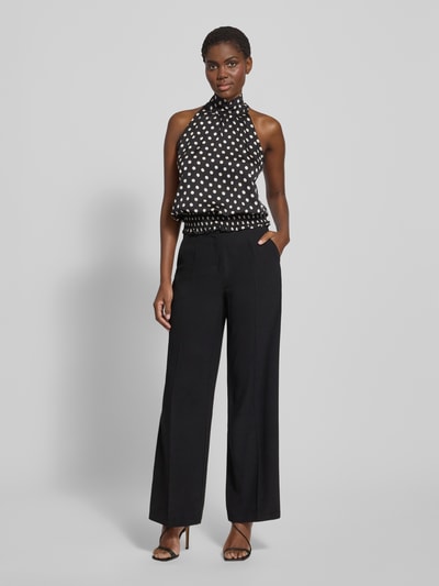 Frauenmodel trägt Blusentop im Allover-Look von Neo Noir, schwarz mit weißen Punkten, Stehkragen, rückseitige Schnürung, Ganzkörperansicht von vorne.