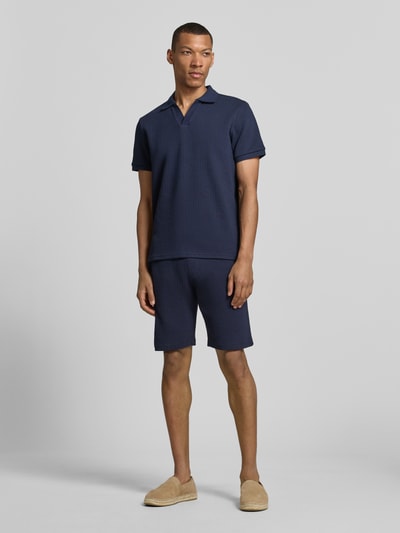Männermodel trägt Regular Fit Strick-Poloshirt mit V-Ausschnitt von MCNEAL, dunkelblauer Baumwoll-Mix mit Stretch-Anteil, Ganzkörperansicht von vorne.