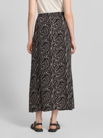 Frauenmodel trägt Ausgestellter Maxi-Rock aus reiner Viskose Modell 'EASY JOY' von Vero Moda, schwarzes Popeline-Gewebe mit grafischem Allover-Muster, elastischer Bund, Ganzkörperansicht Rückansicht.