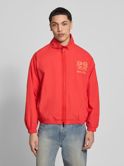 Męski model nosi Segeljacke mit Stehkragen und Logo-Stitching von ANOTHER COTTON LAB, czerwony kolor, bawełna, prosty krój, zamek błyskawiczny dwustronny, wyhaftowane logo, elastyczne wykończenia, długość tyłu w rozmiarze M: 63 cm, szerokość ramion w rozmiarze M: 60 cm, szerokość w klatce piersiowej w rozmiarze M: 63 cm, długość rękawów w rozmiarze M: 55 cm, całkowity widok z przodu.