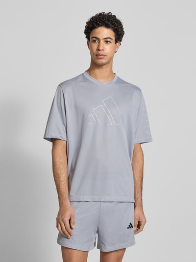 Männermodel trägt T-Shirt mit Label-Print von adidas Training in Hellgrau, Regular-Fit, Rundhalsausschnitt, Ganzkörperansicht von vorne. Rückenlänge bei Größe M: 70 cm.