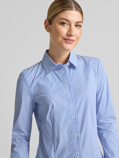 Frauenmodel trägt Hemdbluse aus Baumwoll-Mix von Christian Berg Woman mit blauen und weißen Streifen, taillierte Passform, Nahaufnahme Oberkörper, Baumwoll-Mix mit Stretch-Anteil, langärmeliges Design, 1-Knopf-Manschetten, Rückenlänge 65 cm, Ärmellänge 61 cm.