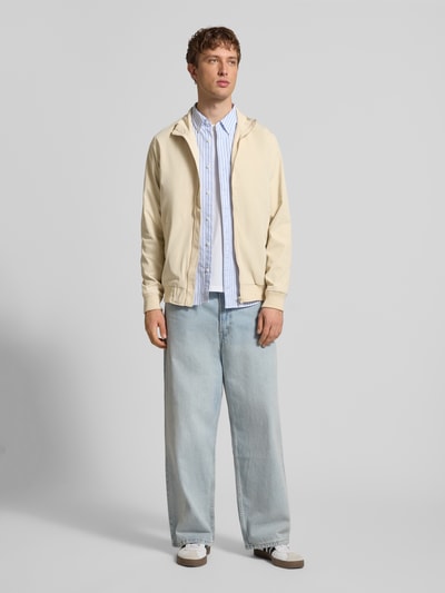 Männermodel trägt Regular Fit Jacke mit Stehkragen Modell 'Hefi' von Blend in Beige, reine Baumwolle, Reißverschluss, Ganzkörperansicht von vorne.