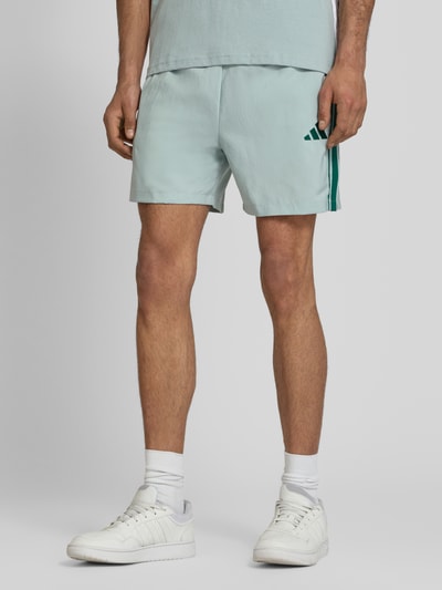 Męski model nosi Regular Fit Sport-Shorts mit Kontraststreifen Modell 'CHELSEA' von adidas Sportswear, jednolity kolor, logo, kieszenie, widok całej sylwetki z przodu.