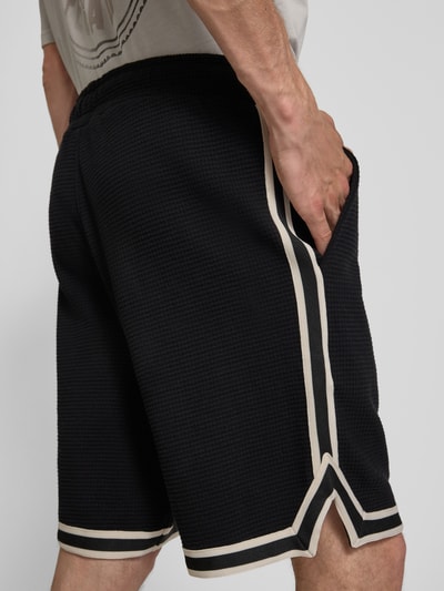 Männermodel trägt Shorts mit Strukturmuster und Label-Stitching von PEGADOR in Schwarz, Baumwolle, Regular-Fit, Eingrifftaschen, Ganzkörperansicht Rückansicht.