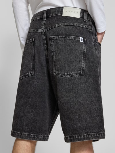 Męski model nosi Worker Shorts im 5-Pocket-Design od Edwin z bawełny, luźny krój, czarne, tekstura jeansowa. Ganzkörperansicht Rückansicht. Szerokość w rozmiarze 32: 45 cm, długość wewnętrzna nogawki w rozmiarze 32: 28 cm.