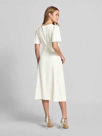 Frauenmodel trägt Cocktailkleid mit Gürtel und Rundhalsausschnitt von Rinascimento im Material-Mix mit Stretch-Anteil, Taillierter Schnitt, Midikleid, Rückenreißverschluss, dezentes Creme, glatte Struktur, Ganzkörperansicht Rückansicht.