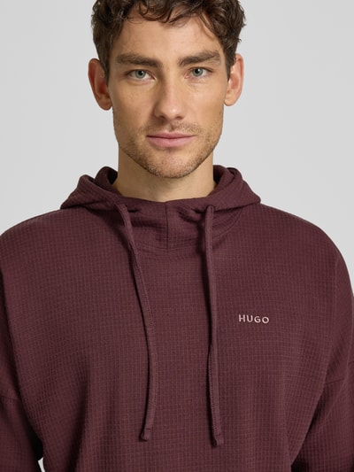 Männermodel trägt Regular Fit Hoodie aus Baumwoll-Mix Modell 'AUSTIN' von HUGO in Bordeaux mit Waffel-Struktur, Nahaufnahme Oberkörper.