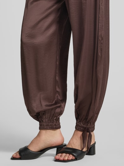 Frauenmodel trägt Loose Fit Stoffhose aus Satin mit Viskose-Anteil von mbyM, braun, gesmokte Beinabschlüsse, Nahaufnahme Unterbeine.