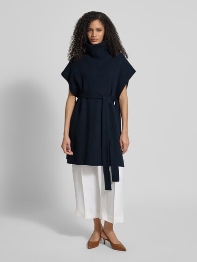 Modelka nosi Regular Fit Poncho aus reiner Schurwolle Model 'FAVANDA' od BOSS, efekt: jednolity kolor, imitacja dzianiny, krój regular fit, aplikacja z logo, wiązany pasek, golf, bez rękawów, czysta żywa wełna; widok całej sylwetki z przodu.