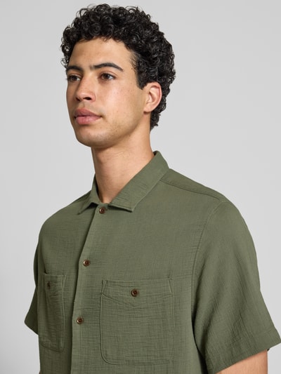 Männermodel trägt Regular Fit Freizeithemd mit Kentkragen und Brusttaschen von Superdry in Oliv, Strukturmuster, Nahaufnahme Oberkörper.