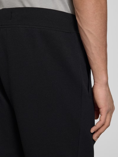 Männermodel trägt Straight Fit Shorts mit Strukturmuster von G-Star Raw, dunkles Strukturmuster, Logo-Detail, Nahaufnahme seitlich.