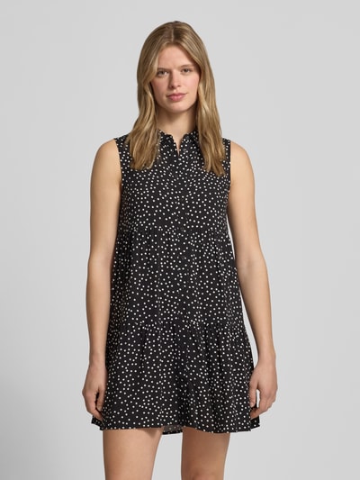 Frauenmodel trägt Ausgestelltes Hemdblusenkleid aus reiner Viskose Modell 'THEA' von Only in Optik:Allover-Muster, Mini-Länge, Hemdblusenkragen, V-Ausschnitt, Raffung, Knopfleiste, ohne Ärmel, gerader Saum, Material: reine Viskose, Schwarz mit weißen Punkten, fließende Textur, Ganzkörperansicht von vorne.