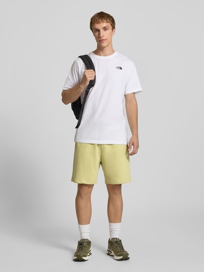 Męski model nosi Sweatshorts mit Logo-Stitching von The North Face w kolorze jasnożółtym, bawełna, krój relaxed fit, elastyczny pas z troczkiem, logo-stitching, szerokość w rozmiarze M: 40 cm, długość nogawki od wewnątrz w rozmiarze M: 18 cm, widok całej sylwetki z przodu.