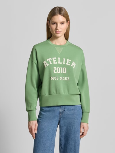 Kobiece model prezentuje Relaxed Fit Sweatshirt aus Viskose-Mix Modell 'Nima' od MOS MOSH, zielona, logo, okrągły dekolt, elastyczne wykończenia, mieszanka wiskozy, widok całej sylwetki z przodu.