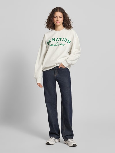 Modelka kobieca ma na sobie Sweatshirt mit Label-Stitching und Rundhalsausschnitt od P.E Nation, bawełniana mieszanka, krój relaxed fit, prążkowany dekolt, zielony nadruk, szerokie ramiona, ściągacze, widok całej sylwetki z przodu.