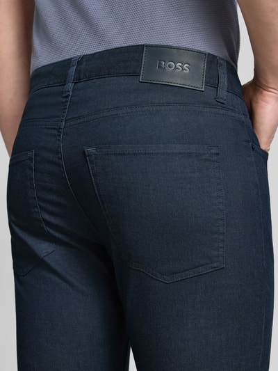 Männermodel trägt Slim Fit Modell Chino aus Baumwoll-Mix 'DELAWARE5' von BOSS in Dunkelblau, 5-Pocket-Design, Label Patch, Nahaufnahme Rückansicht.