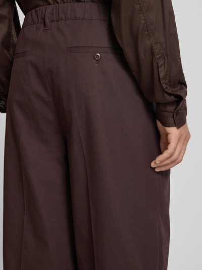 Männermodel trägt Wide Fit Hose aus reiner Baumwolle von Filippa K in Braun mit Bügelfalten, Gesäßtaschen, Nahaufnahme Rückansicht.
