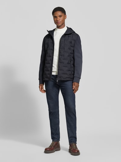Männermodel trägt Regular Fit Steppjacke mit winddichter Funktion von Strellson in Dunkelblau, kombiniert mit Jeans, Ganzkörperansicht von vorne, Herren Steppjacke von Strellson.