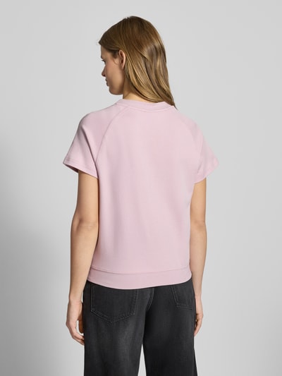 Modelka nosi Regular Fit T-Shirt mit Logo-Patch Modell 'Raglan' von G-Star Raw, różowy kolor, krój regular fit, czysta bawełna, okrągły dekolt, elastyczne wykończenie, długość tyłu w rozmiarze S: 57 cm, widok całej sylwetki z tyłu.