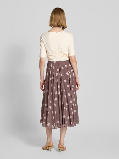 Vrouwenmodel draagt Midikleid in Falten-Optik van Christian Berg Cocktail met elastische materiaalmix, getailleerde fit, plooidetail, ruches, halve mouw, bruin met witte stippen, textuurmix, geheellichaamsaanzicht achteraan.