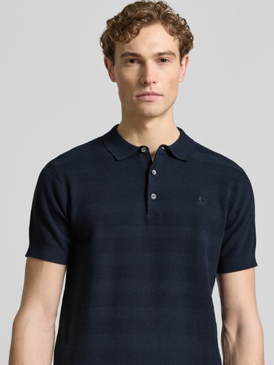 Mężczyzna prezentuje Slim Fit Poloshirt mit Logo-Stitching von Lerros z bawełny, krój slim fit, krótka lista guzików, kolor granatowy, logo na piersi, widok na górną część ciała z przodu.