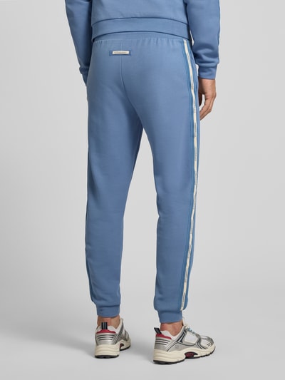 Männermodel trägt Sweatpants mit elastischem Bund von EA7 Emporio Armani in Blau mit weißen Streifen, Baumwoll-Mix, Ganzkörperansicht Rückansicht.