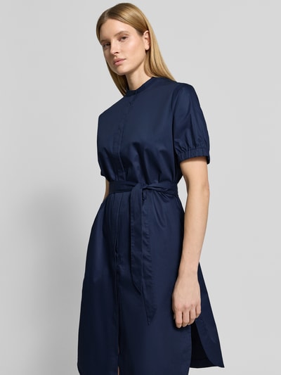 Modelka kobieta nosi Regular Fit Kleid mit Stehkragen od Fynch-Hatton, granatowy, bawełniany, krój regular fit, krótki rękaw, elastyczne mankiety, odpinany pasek, pełny plisa guzikowa, kieszenie na biodrach, długość tyłu w rozmiarze 36: 105 cm, szerokość w rozmiarze 36: 59 cm, długość rękawa w rozmiarze 36: 27 cm, ujęcie całej sylwetki z przodu.