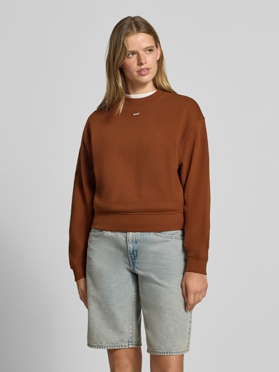 Frauenmodel trägt Regular Fit Sweatshirt aus reiner Baumwolle Modell 'Delessa_B' von HUGO in Braun, kombiniert mit hellblauer Jeansshorts, Damen Sweatshirt von HUGO Blue, Ganzkörperansicht von vorne.
