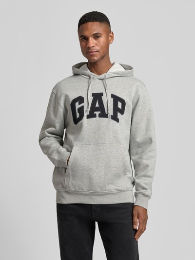 Männermodel trägt Hoodie mit Logo und Känguru-Tasche von GAP in Grau, Baumwoll-Mix, Regular Fit, Ganzkörperansicht von vorne.