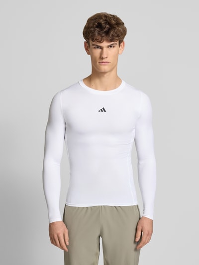 Männermodel trägt Longsleeve mit Label-Print von adidas Training in Weiß, enger Slim Fit, Rundhalsausschnitt, Material-Mix mit Stretch, Ganzkörperansicht von vorne.
