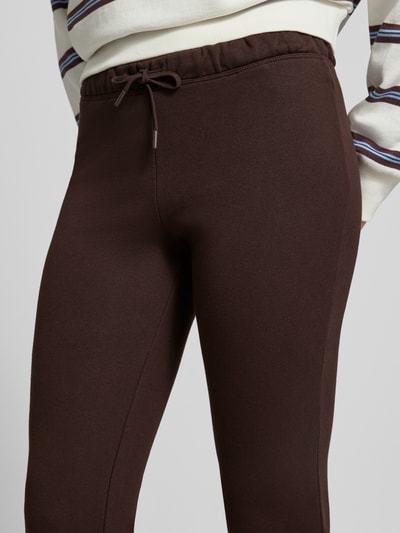 Frauenmodel trägt Flared Sweatpants aus reiner Baumwolle von REVIEW in Dunkelbraun mit elastischem Bund und Tunnelzug, Nahaufnahme Oberkörper.