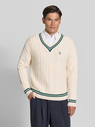 Männermodel trägt Strickpullover mit Zopfmuster von REVIEW in Creme mit grünem Kontraststreifen und gerippten Abschlüssen, Ganzkörperansicht von vorne.