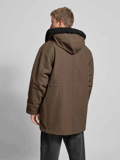 Männermodel draagt Regular fit Parka met Logopatch model 'Siberia' van Carhartt, bruin, capuchon met tunnelkoord, klepzakken, ruglengte 88 cm, schouderbreedte 47 cm, borstwijdte 64 cm, mouwlengte 65 cm, Ganzkörperansicht Rückansicht.