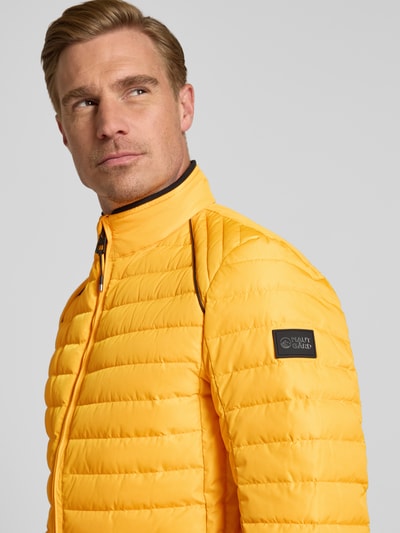 Männermodel trägt Regular Fit Jacke in Stepp-Optik Modell 'OLYMPUS' von NAUTGÅRD in Gelb, Stehkragen, Reißverschluss, Nahaufnahme Oberkörper.