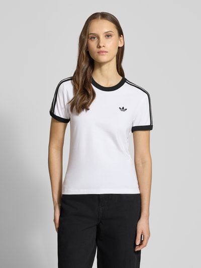 Frauenmodel trägt Slim Fit T-Shirt aus Baumwoll-Mix von adidas Originals, weiß mit schwarzen Details, Rundhals, kurzärmelig, Ganzkörperansicht von vorne.
