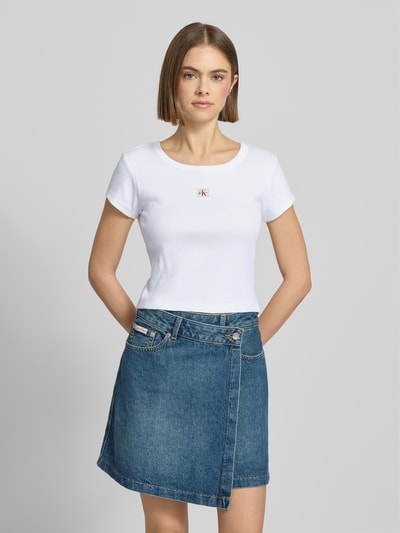 Modelka kobieca nosi Cropped T-Shirt mit Label-Detail od Calvin Klein Jeans, biały kolor, bawełna z elastanem, okrągły dekolt, widok z przodu, ujęcie całej sylwetki.