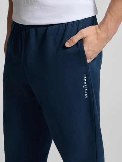 Männermodel trägt Regular Fit Sweatpants aus Baumwoll-Mix von Tommy Jeans in Optik: Unifarben, Label-Stitching-Applikation, Nahaufnahme Oberkörper.