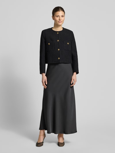 Frauenmodel trägt Regular Fit Blazer mit Rundhalsausschnitt Modell 'MEREDITH' von Bash aus reiner Baumwolle, schwarzer Stoff, goldene Knöpfe, aufgesetzte Brusttaschen, Knopfleiste, glatte Textur, Ganzkörperansicht von vorne.