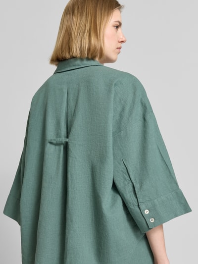 Frauenmodel trägt Boxy Fit Bluse mit V-Ausschnitt Modell 'Lava' von FREE/QUENT aus grünem Leinen-Viskose-Mix, strukturierte Oberfläche, 3/4-Arm, Rückenansicht, Nahaufnahme Oberkörper.